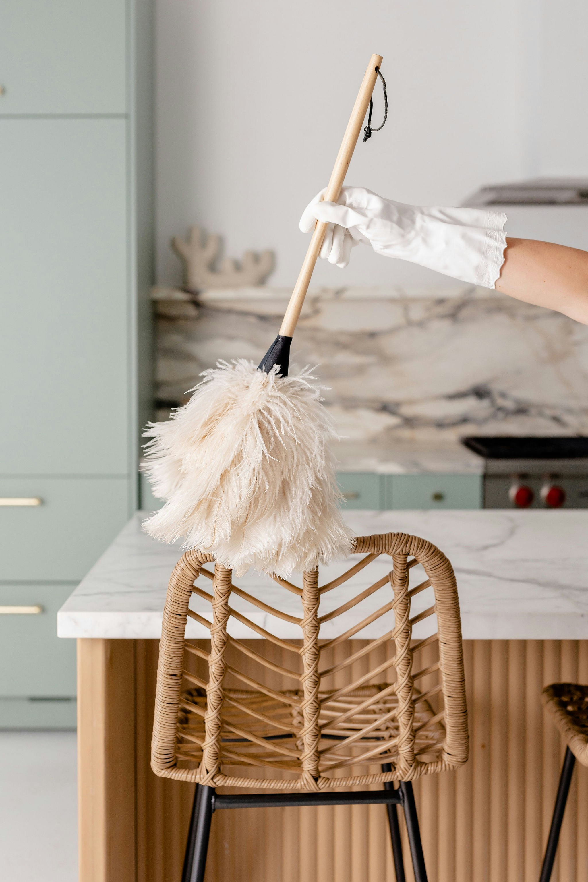 A gloved hand dusting a rattan stool beside a kitchen island